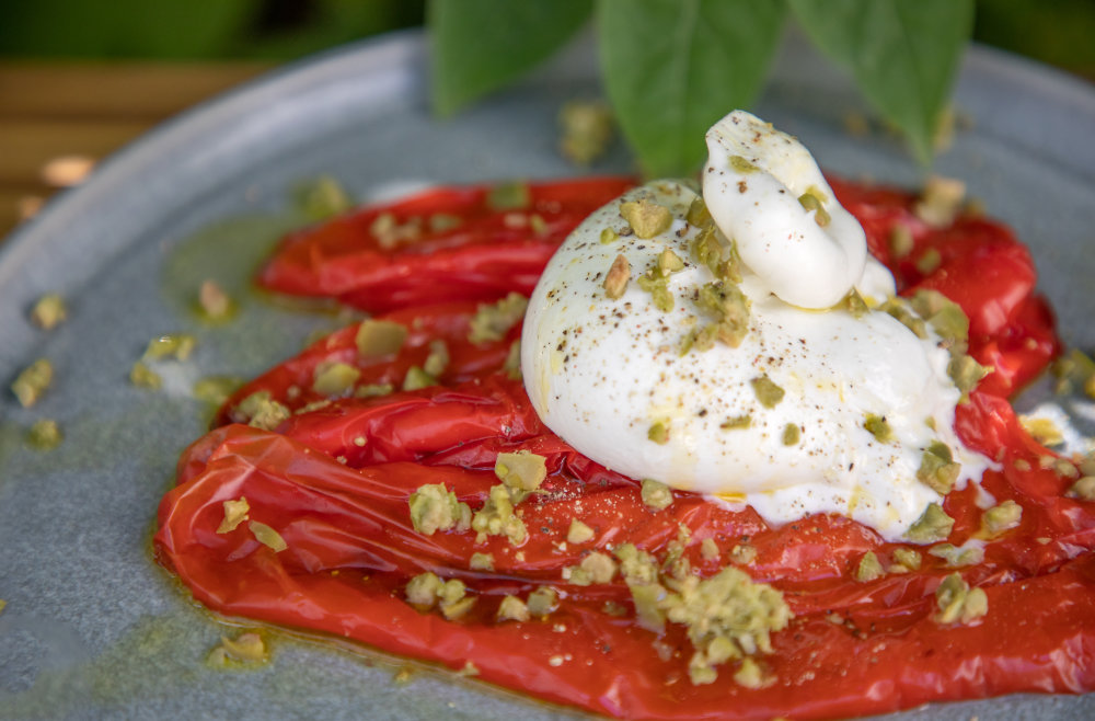rote paprika auf teller mit burrata und olivenbrösel